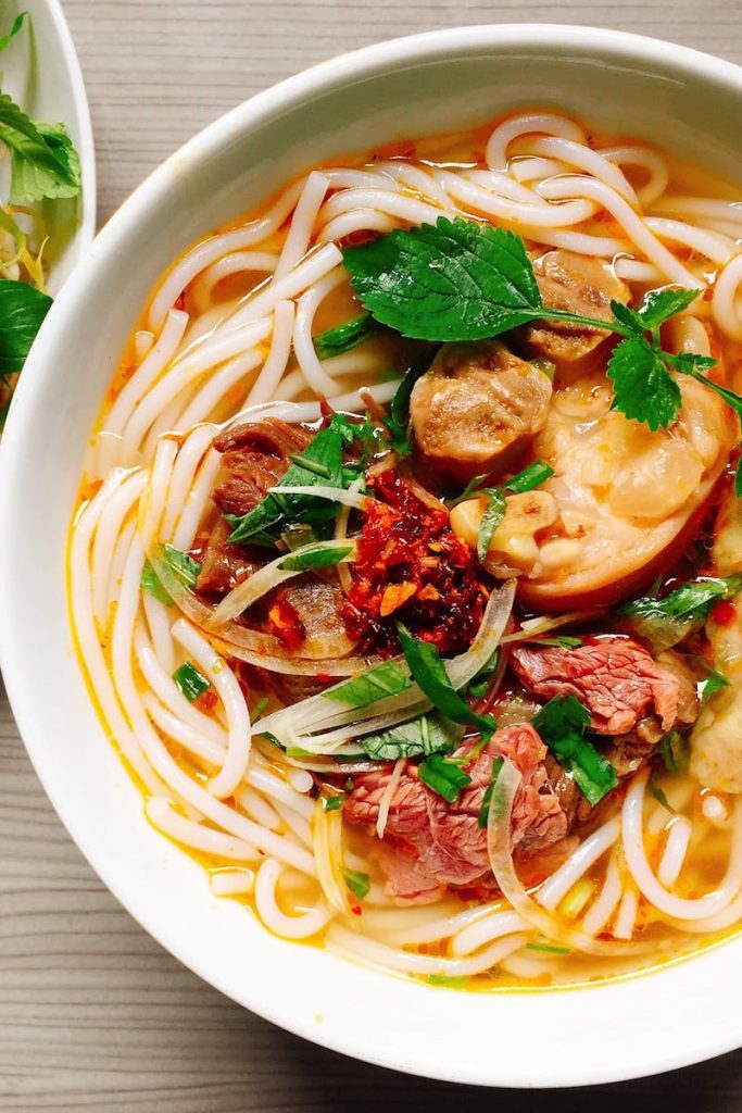 A colorful bowl of Vietnamese noodle soup with fresh herbs and vegetables.